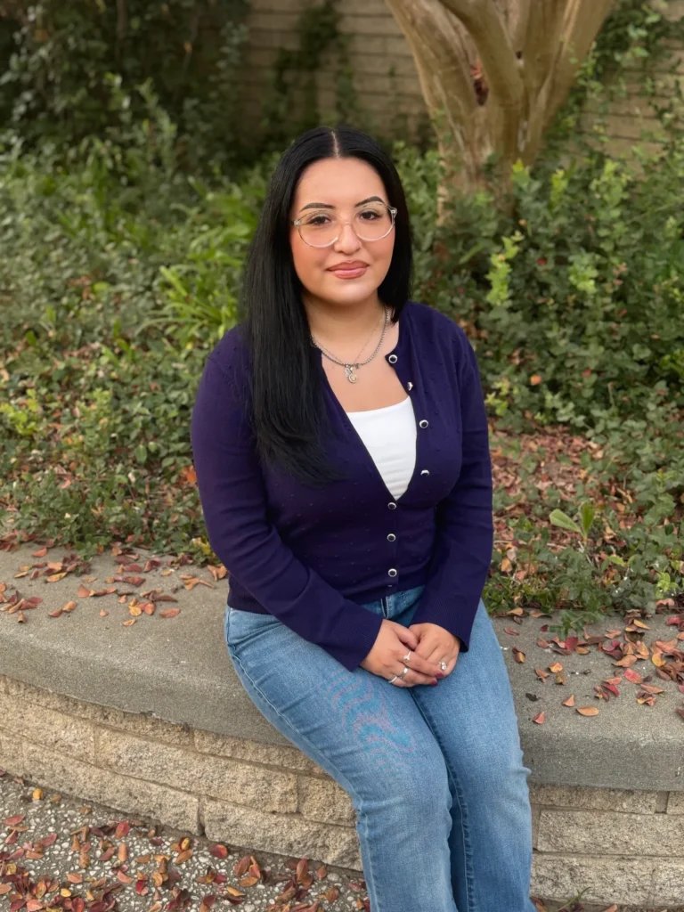 A smiling woman sitting outdoors on a concrete bench.